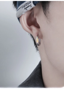 Macro shot of silver ear hoop featuring a gold cross relief pattern on male model