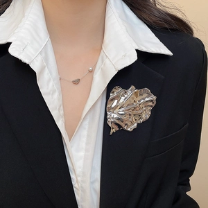 Macro detail of a large silver wrinkled leaf brooch and pearl necklace on a black blazer