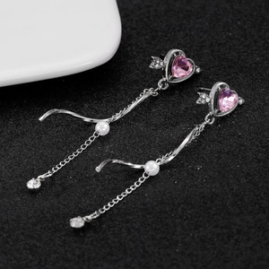 Macro view of pink heart crystal earrings with wing details and long chain drops