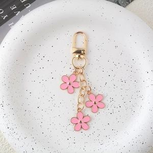 Detail view of gold keychain featuring three pink enamel flowers on a white plate