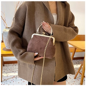 Pochette en velours marron avec poignée en perles et chaîne dorée tenue par un modèle