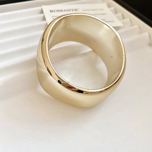 Gros plan d'un bracelet large en acrylique doré minimaliste avec un effet miroir poli