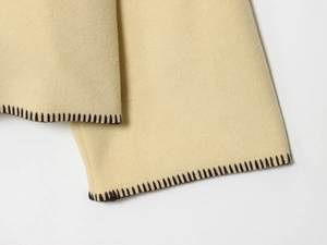 Detail of beige wool texture with decorative dark whipstitch edge on a cozy jacket