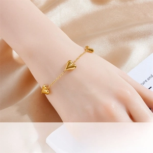 Close-up of gold plated stainless steel heart charm bracelet worn on wrist with silk