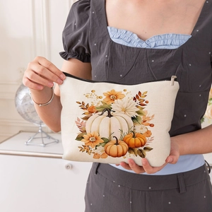 Linen makeup bag with autumn pumpkin print and black zipper held by hand at home