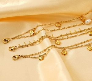 Detail of 18K gold-plated stainless steel bracelet featuring heart charms and pearl