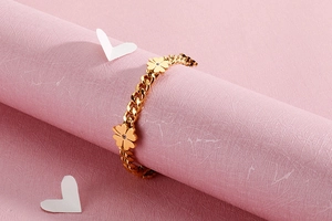 Detail of gold four-leaf clover bracelet with zircon studs on pink textured background