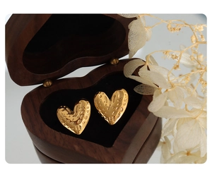 Detail of golden heart earrings with hammered texture in a dark wooden jewelry box