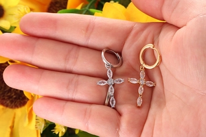 Close-up of hand holding gold and silver cross earrings with marquise-cut white zircons