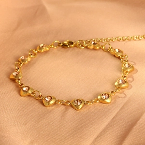 Macro detail of a golden heart-shaped bracelet with champagne zircons on satin