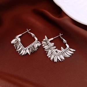 Detailed view of layered silver leaf earrings with textured veins on red silk