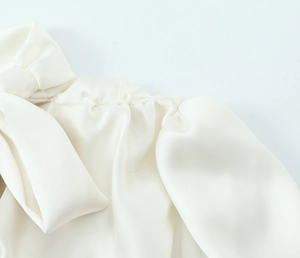 Detailed view of white satin fabric with elegant shoulder bow and ruched detailing