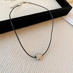 Macro detail of silver star pendant with hammered texture and black cord necklace