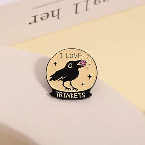 Macro detail of a black crow enamel pin holding a pink gem with I LOVE TRINKETS text