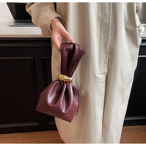 Detail of burgundy PU leather handbag with elegant pleated handle and gold oval buckle