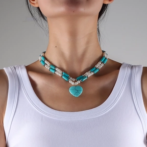 Detail of layered turquoise and pearl necklace with a vintage heart-shaped pendant