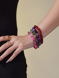 Detail of multi-color natural stone beaded bracelets and gold rings on model's wrist