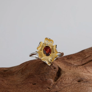 Macro shot of silver ring with gold petals and oval red gemstone on wood background