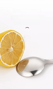 Macro detail of high-mirror polishing on a stainless steel dessert spoon with lemon reflection