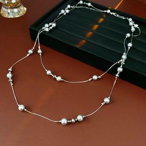 Detail of layered silver-tone necklace with white pearls and grey beads on jewelry tray