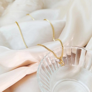 Détail d'un collier en chaîne maille miroir dorée avec un petit pendentif lettre a