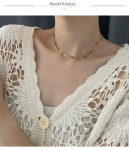 Close-up of colorful daisy enamel charms on a delicate gold chain worn by a model