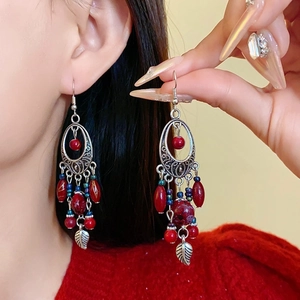 Detail of bohemian red beaded tassel earrings with silver leaf charms on a model