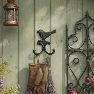 Vintage Wandhaken aus Gusseisen mit Vogelmotiv an einem grünen Holzzaun im Garten