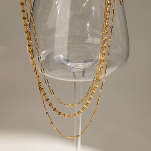 Detailed view of triple-layered golden stainless steel necklace on a wine glass