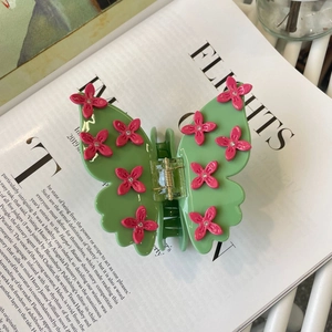 Detail of green butterfly hair claw clip with pink flowers and crystals on a book