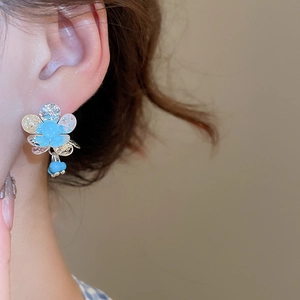 Detailed view of silver flower earrings with blue enamel petals and dangling beads on model