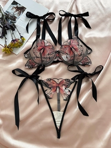 Macro view of butterfly embroidery and satin ribbon ties on sheer black mesh lingerie set