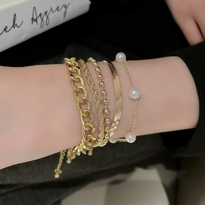 Detail of five-piece gold layered bracelet set with pearls and diverse chain styles