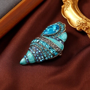Macro shot of seashell brooch with blue rhinestones and green enamel on satin