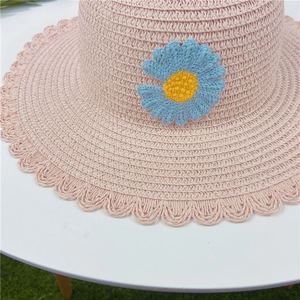 Gros plan d'un chapeau de paille rose tissé avec détail de marguerite bleue tricotée