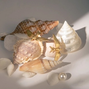 Elegant 18k gold stainless steel swallow earrings displayed with seashells and pearls