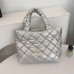 Detail of silver quilted tote bag with metallic finish and metal logo plaque on front