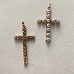 Dettaglio di ciondoli a croce con zircone bianco e perla in finitura dorata
