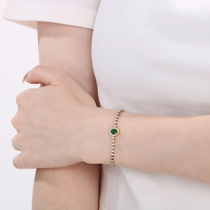 Elegant gold titanium bracelet with emerald stone and diamond halo worn on wrist