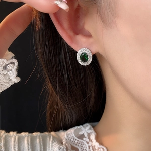 Détail de boucles d'oreilles vintage vert émeraude portées sur une oreille de femme
