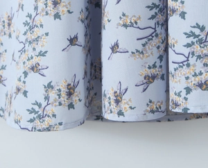 Detail of light blue fabric with white flower clusters and bee patterns on dress hem