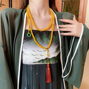 Détail du collier de perles jaunes avec anneau de jade vert et pompon en soie rouge