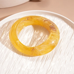 Macro detail of amber resin bangle showing marbled texture on a white ceramic plate