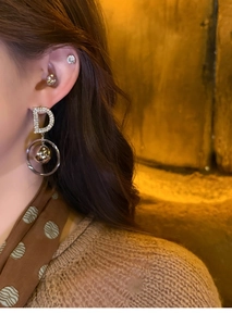 Macro shot of silver letter D earring with pavé rhinestones and a gold bead drop charm