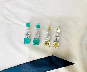 Macro detail of emerald and yellow square-cut crystal drop earrings on silk