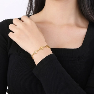 Detail of a gold clover charm bracelet with openwork design worn on a model's wrist