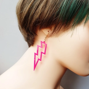 Pink acrylic lightning bolt earrings with gold hooks worn by a female model