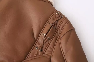 Détail macro d'une veste en similicuir marron avec laçage à l'épaule et œillets métalliques