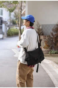 Detailed side view of a large black canvas messenger bag worn with casual streetwear