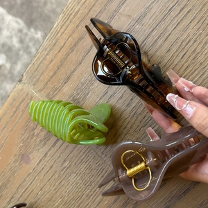 Close-up of three large resin hair claws in amber, green, and pink with metal springs